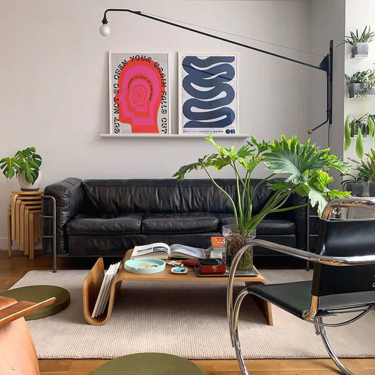 Black leather sofa, abstract pink and blue art, plants, and a chrome chair